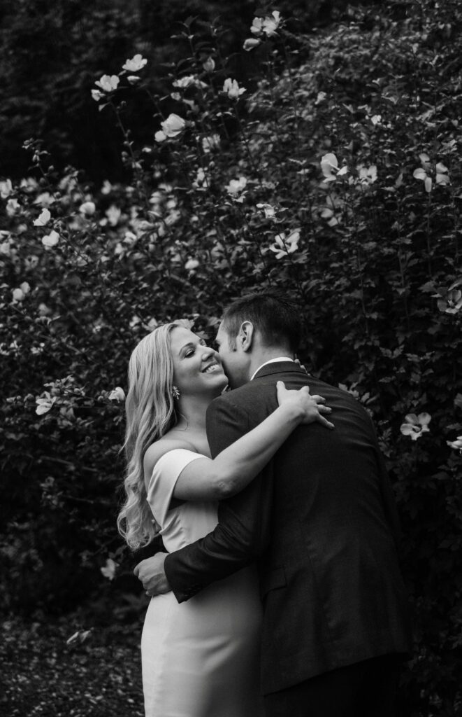 wedding photographer captures a pair of newlyweds in an embrace in front of a flowering bush