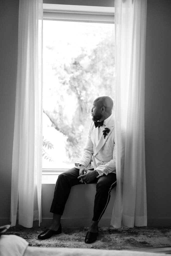 a wedding photographer captures a candid of a groom looking out a window