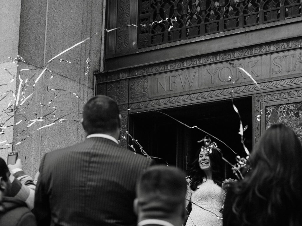 wedding photographer 's photo of a woman stepping out of a new york state city hall beaming as her friends and family throw streamers