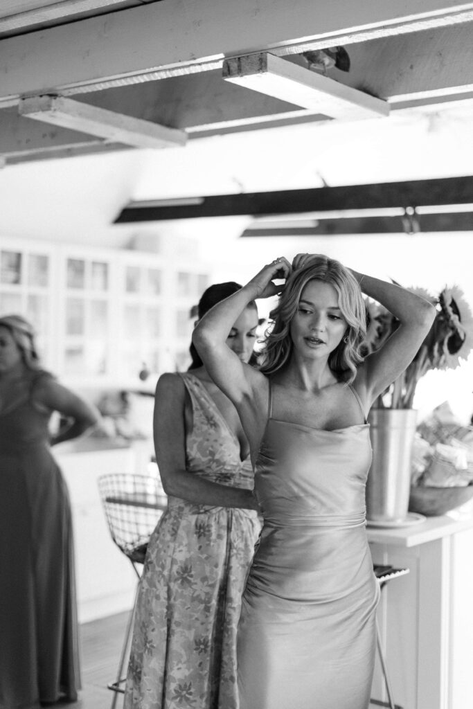 woman wearing a light dress is zipped up as she fixes the back of her hair in this photo from a wedding photographer