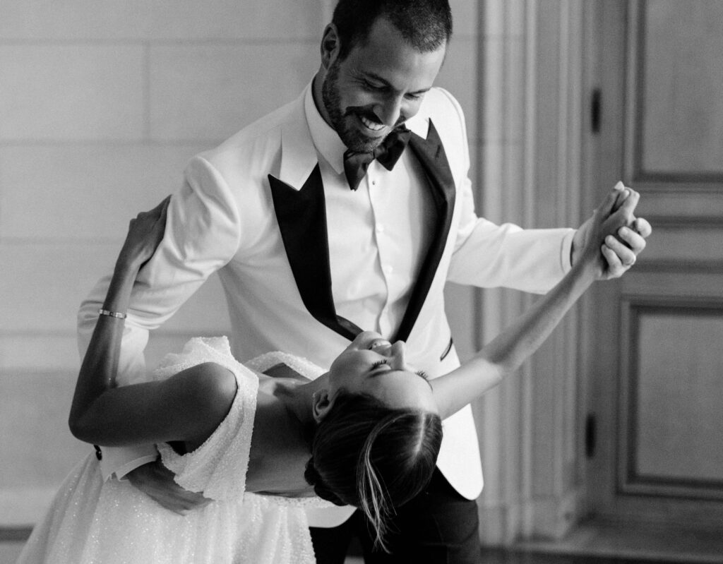 groom smiles at the bride he is dancing with as he dips her during photos with a wedding photographer