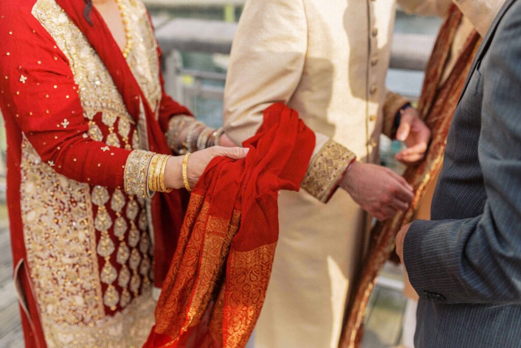 a woman holds a piece of fabric wrapped around a man's arm during a south asian wedding