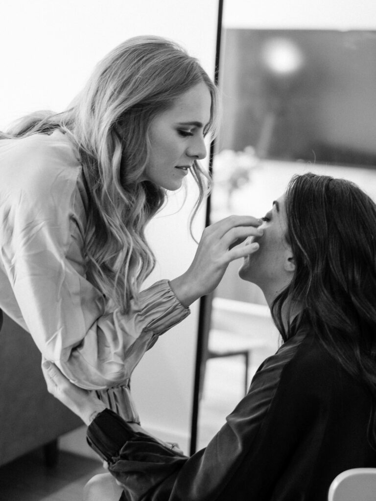 a woman touches another woman's face while getting ready