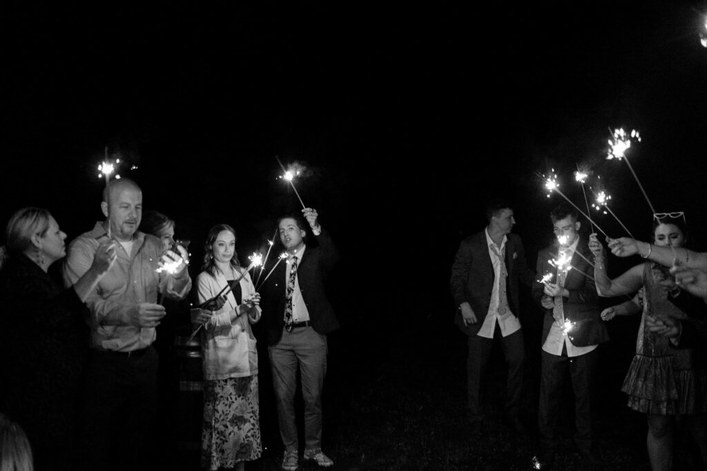 a collection of wedding guests hold sparklers in front of the wedding photographer