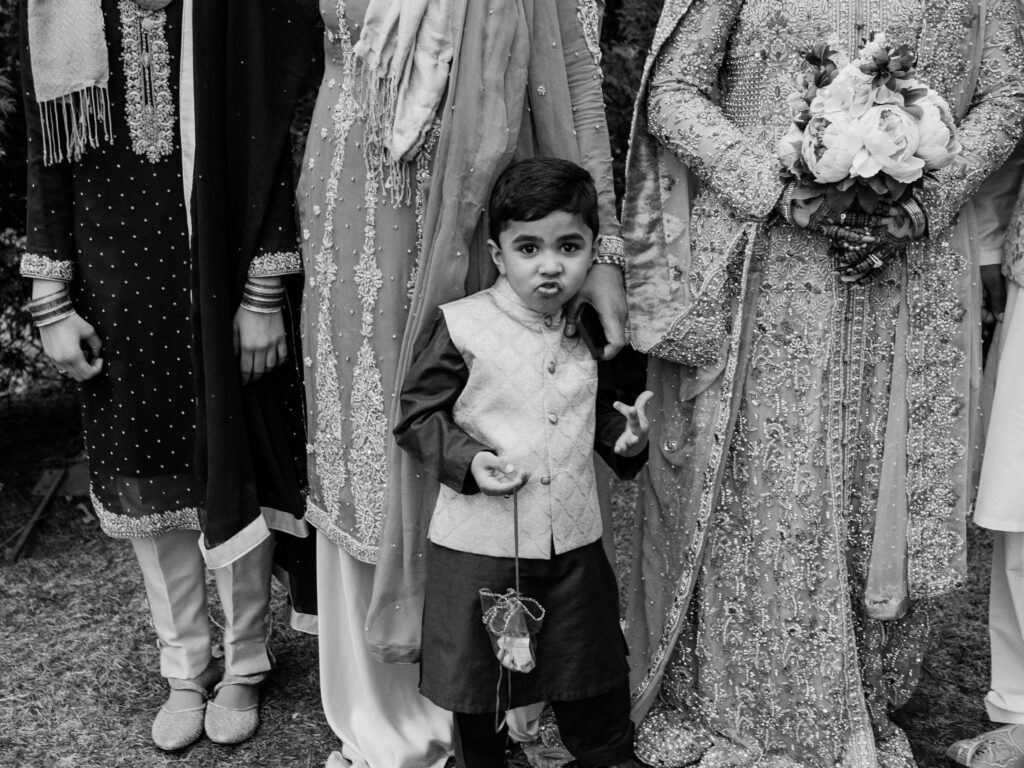 a boy makes a silly face among wedding goers at a south asian wedding