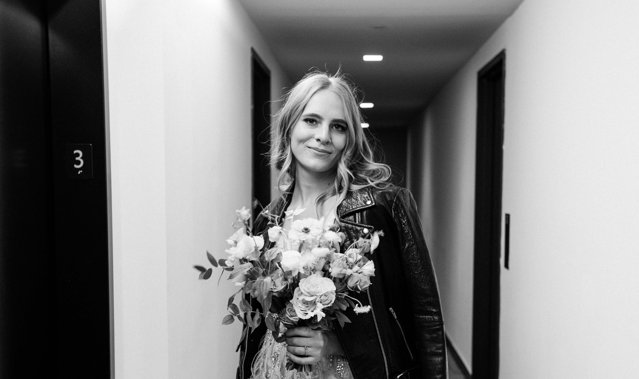 black and white image of chic and queer bride wearing a leather jacket over her wedding gown by new york wedding photographer